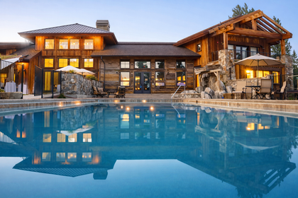 Luxury lodge with lit windows reflected in a calm blue swimming pool at dusk