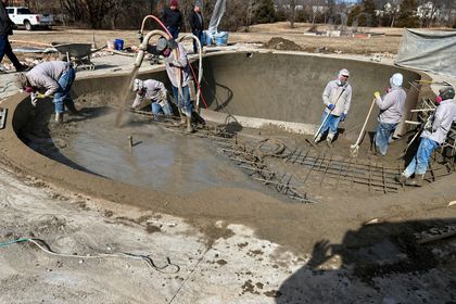 Construction workers spraying wet concrete into a pool
