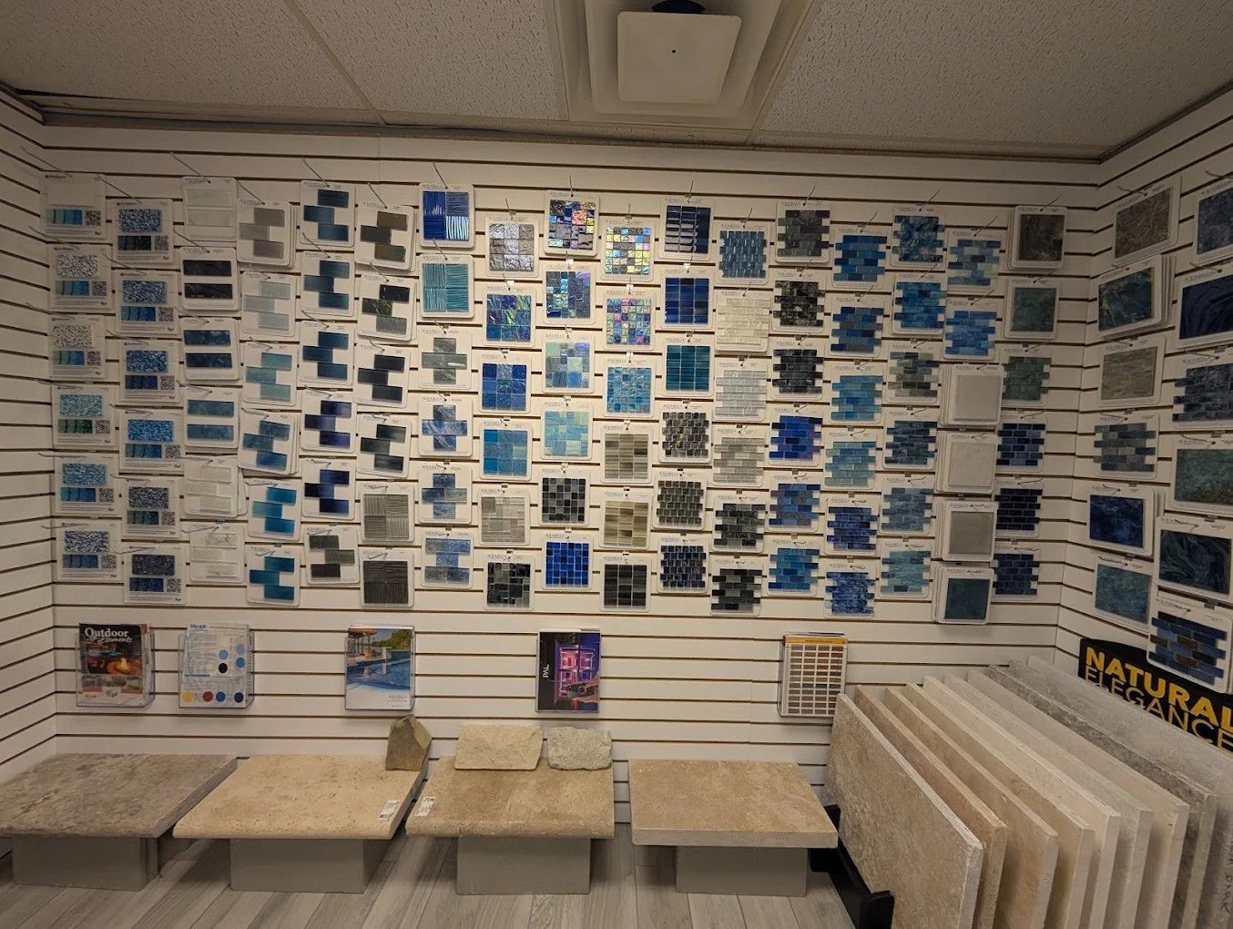 Gallery wall covered with blue and white postcards above beige benches and stacked prints