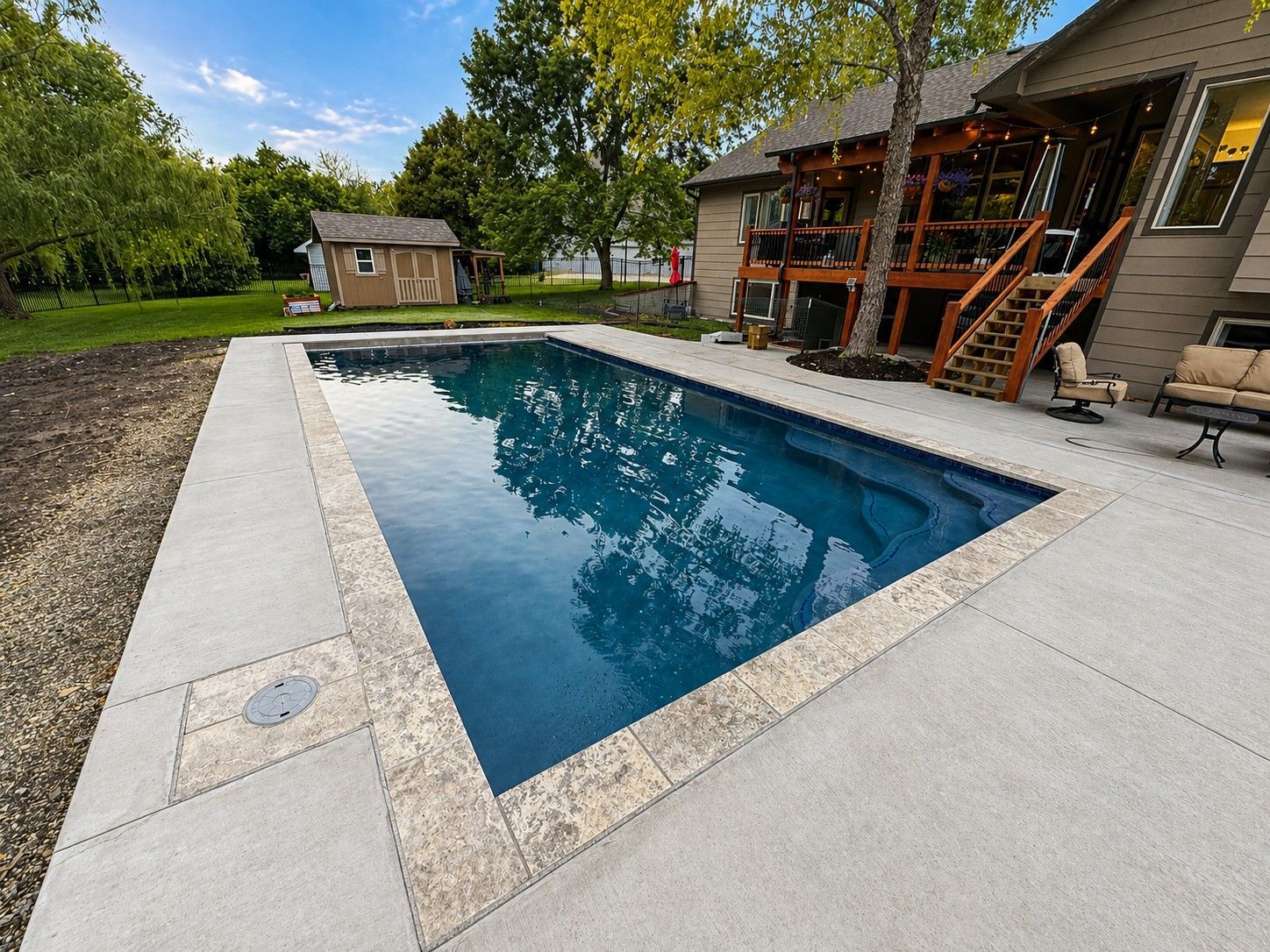 Modern backyard with rectangular in-ground swimming pool beside a house and trees