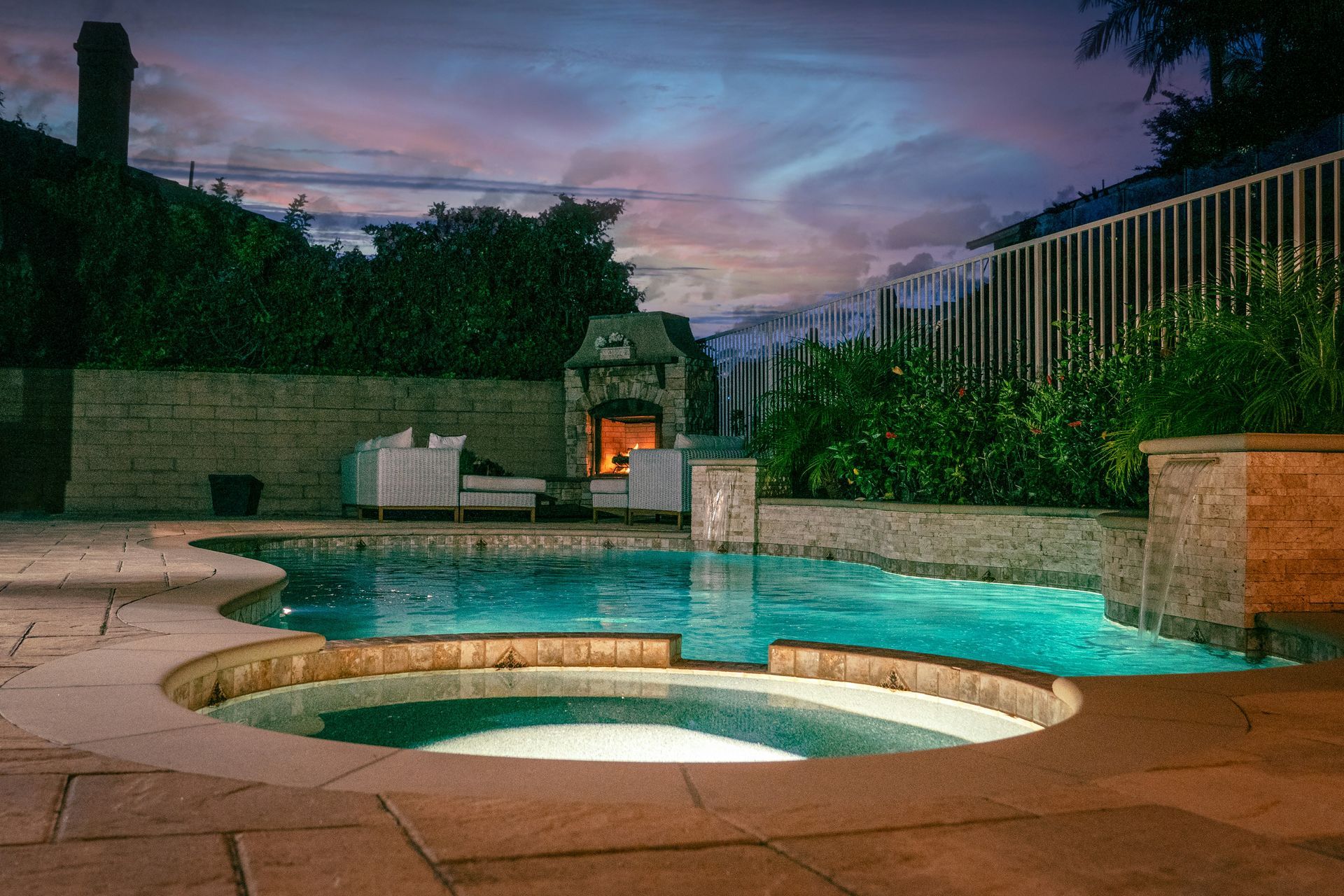 Backyard pool and hot tub at dusk with turquoise water and stone patio