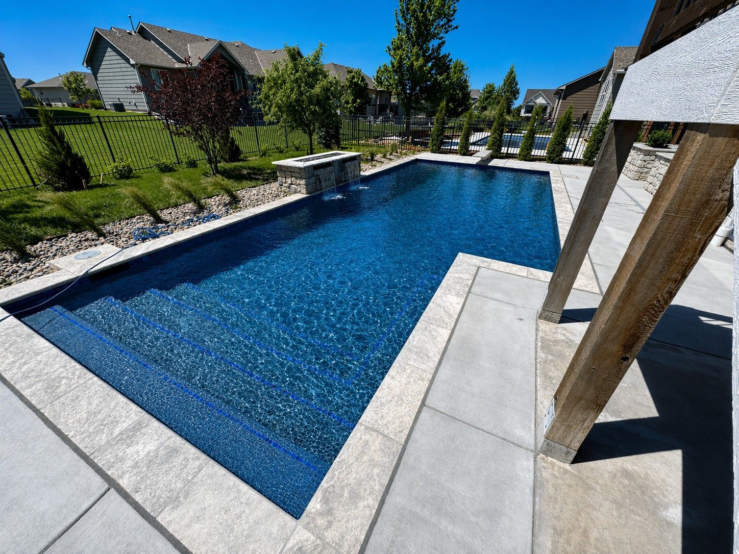 Rectangular blue backyard pool with a small waterfall