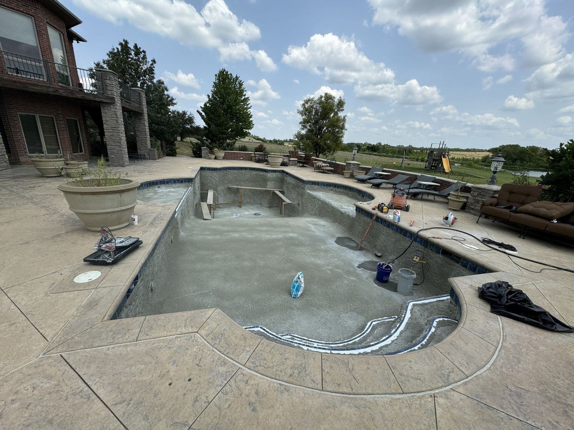 Empty backyard swimming pool under construction beside a stone patio and house
