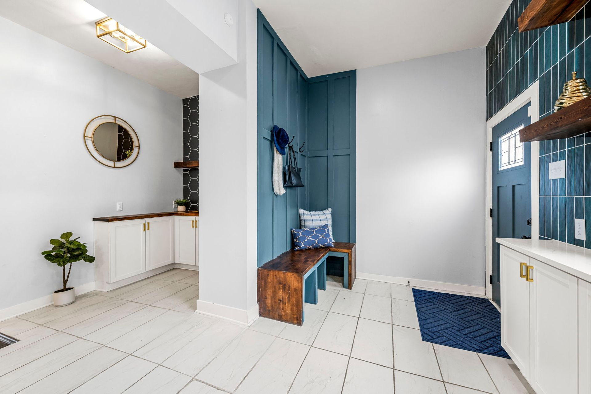 Entryway with white floor tiles, blue accent wall, wooden bench, and a front door with blue tile surround.