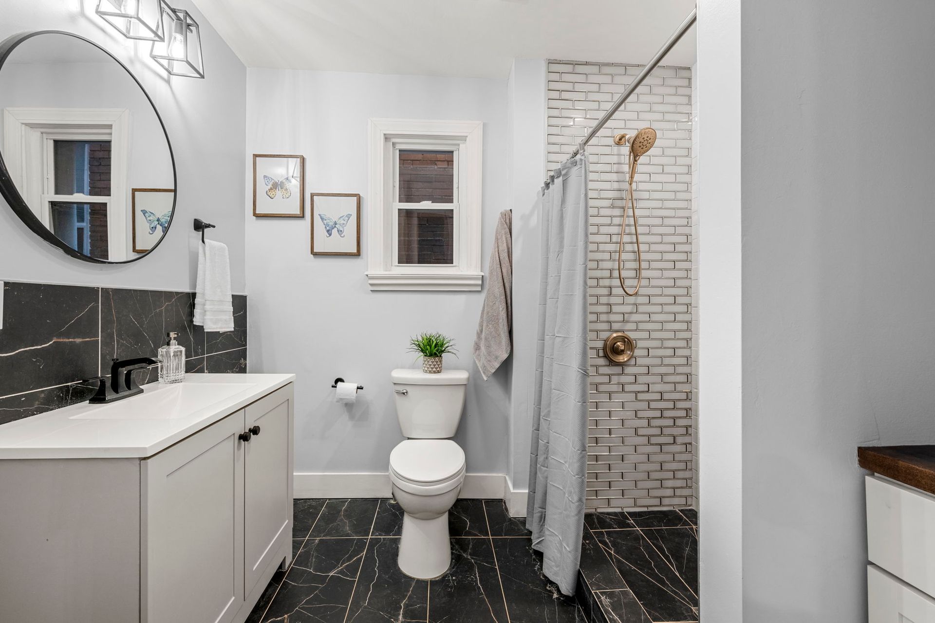 Modern bathroom with white vanity, toilet, and shower, black and white tiled floor, brick shower wall.