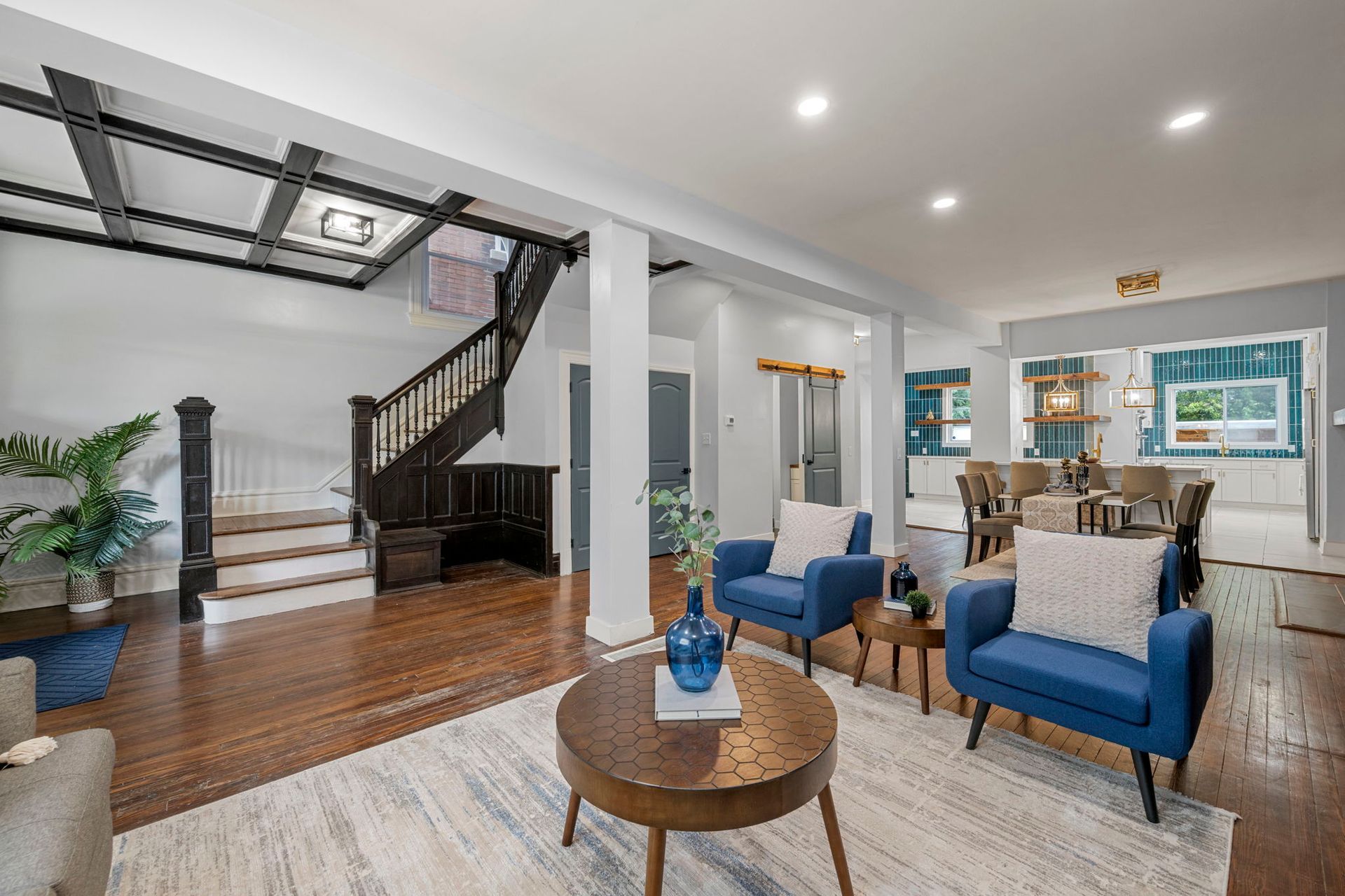 Living room with blue chairs, wooden table, and dark wooden staircase.