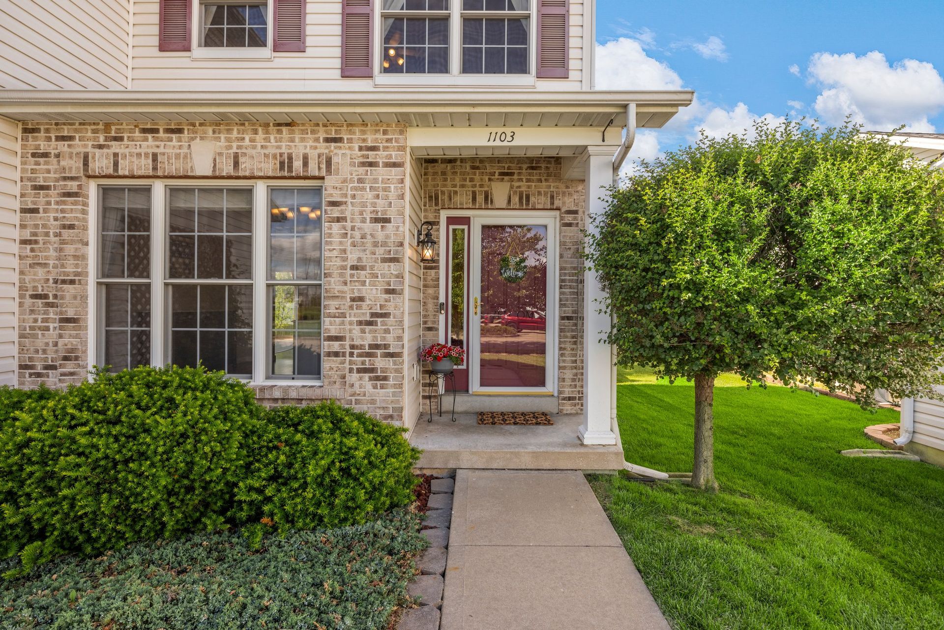 The front of a brick house with a porch and a walkway leading to it.