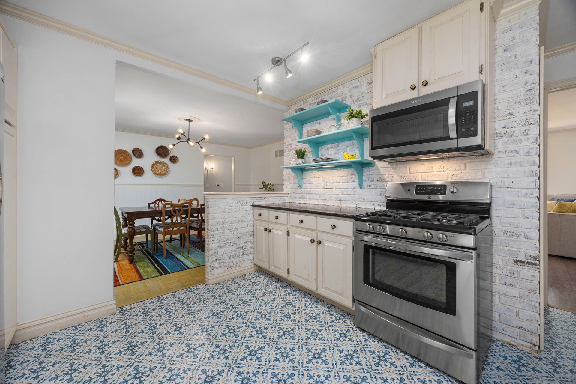 Kitchen with blue patterned floor, white brick-like wall, stainless steel appliances, and open view to dining area.