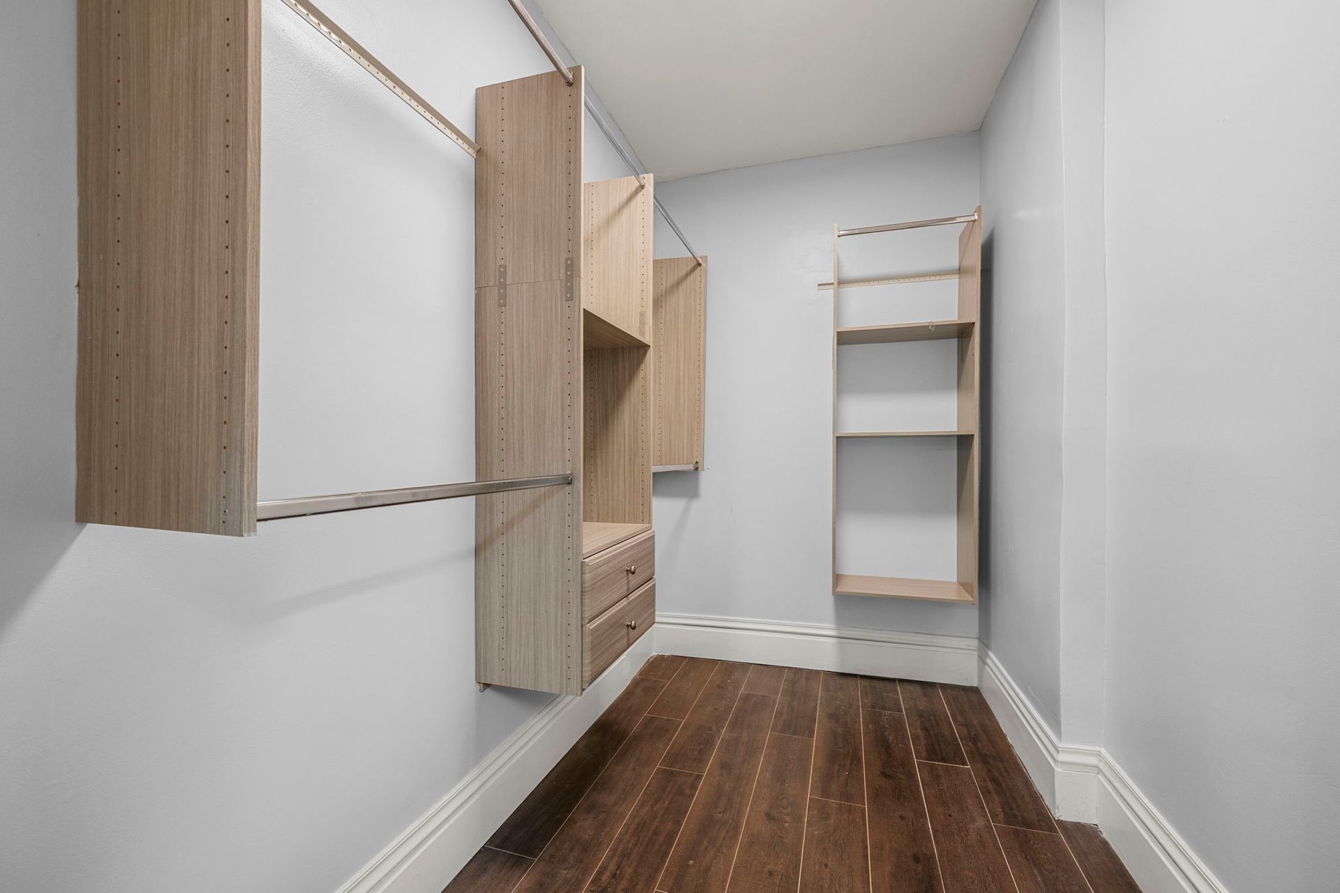 Walk-in closet with light wood shelves and dark wood floor, gray walls.