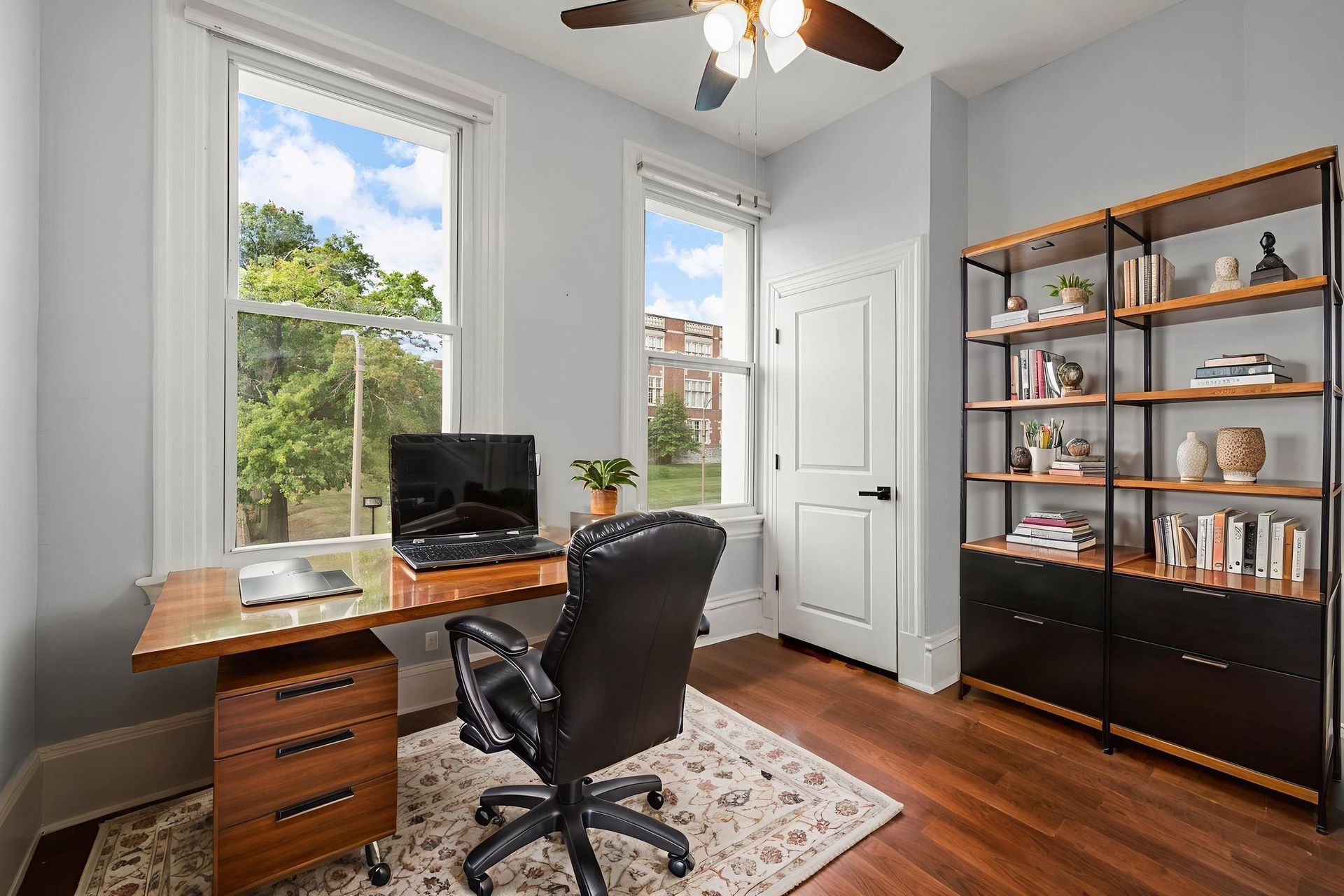 Home office with desk, chair, and bookshelf near windows.