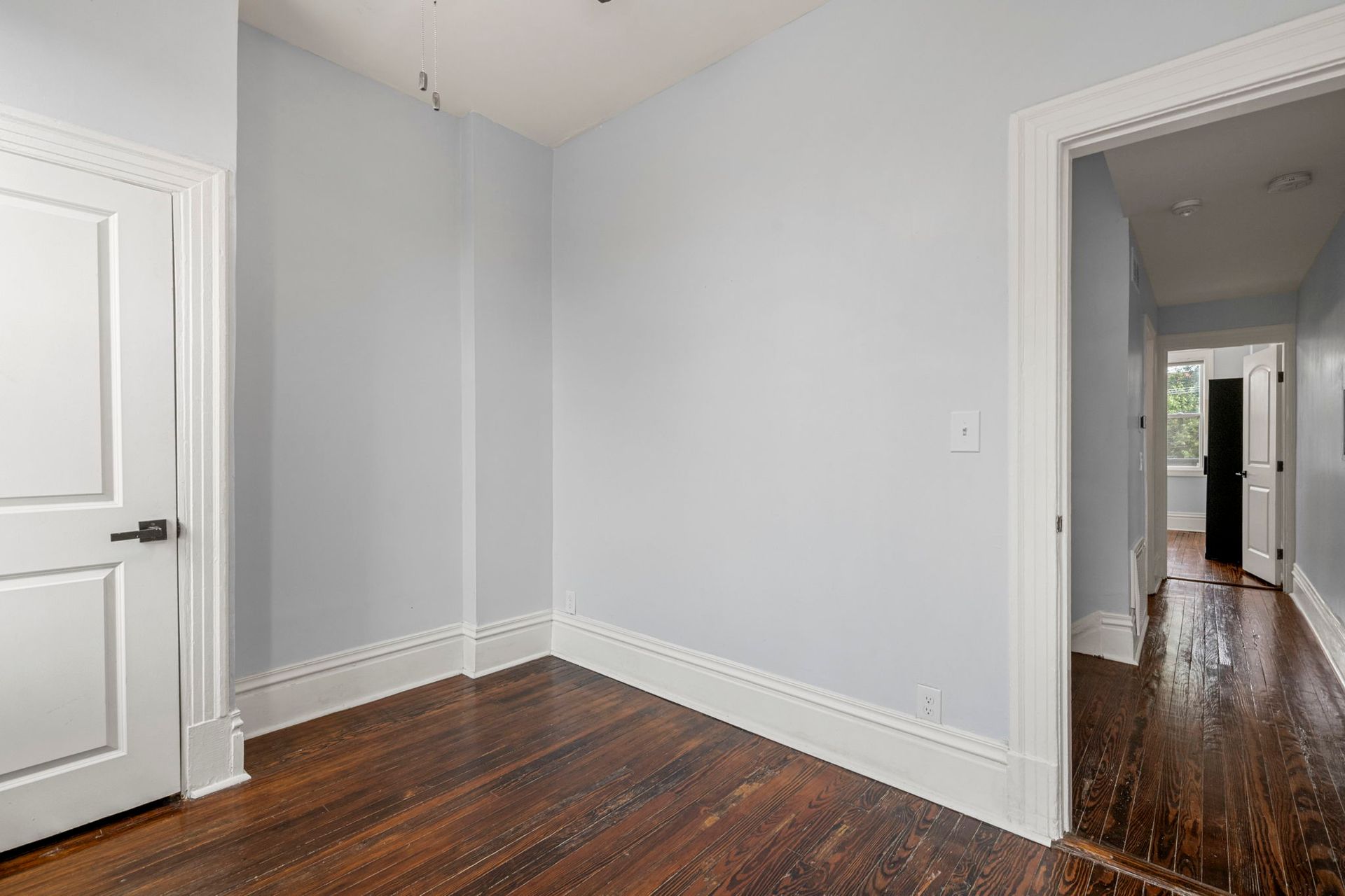 Empty room with blue walls, white trim, dark wood floors, and an open doorway.