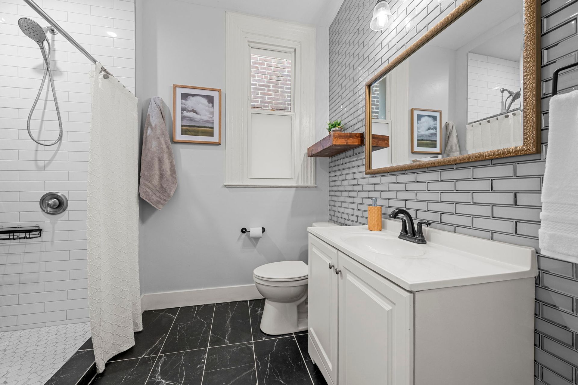 Bathroom with white vanity, black tiled floor, white and gray brick-like tile, and framed mirror.