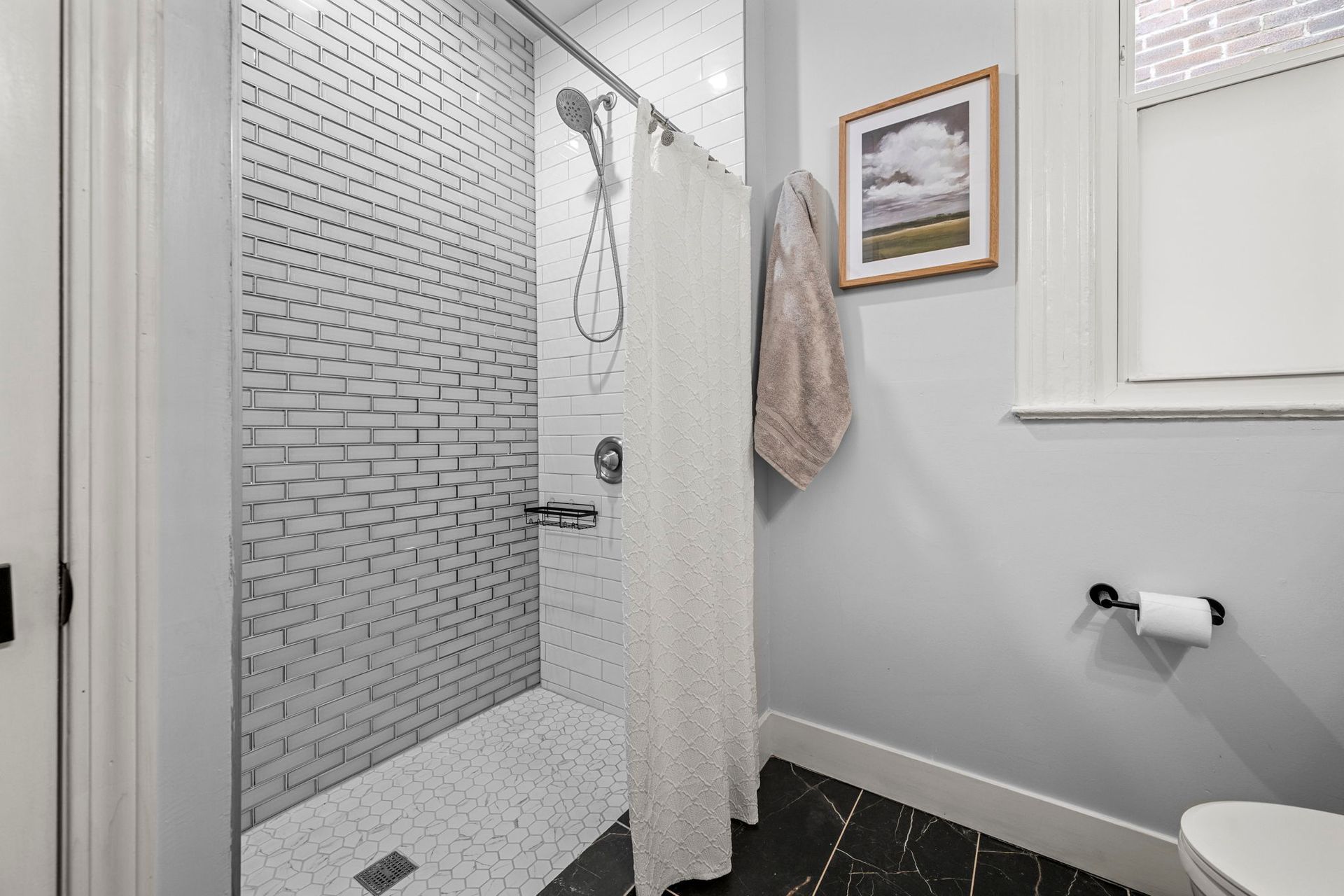 Bathroom with tiled shower, shower curtain, framed art, towel, and toilet paper roll.