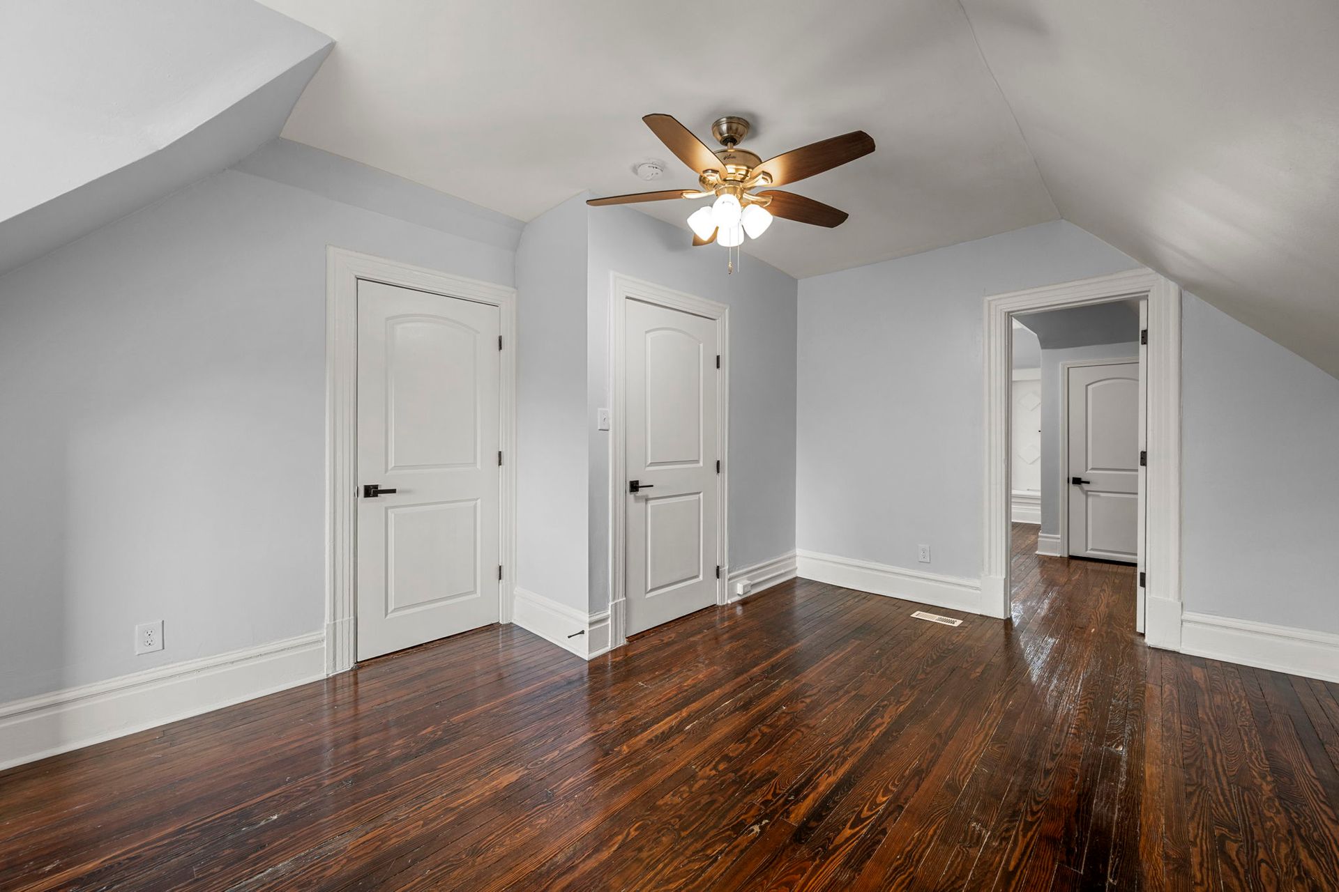 Bedroom with hardwood floor, light blue walls, white doors, and a ceiling fan.