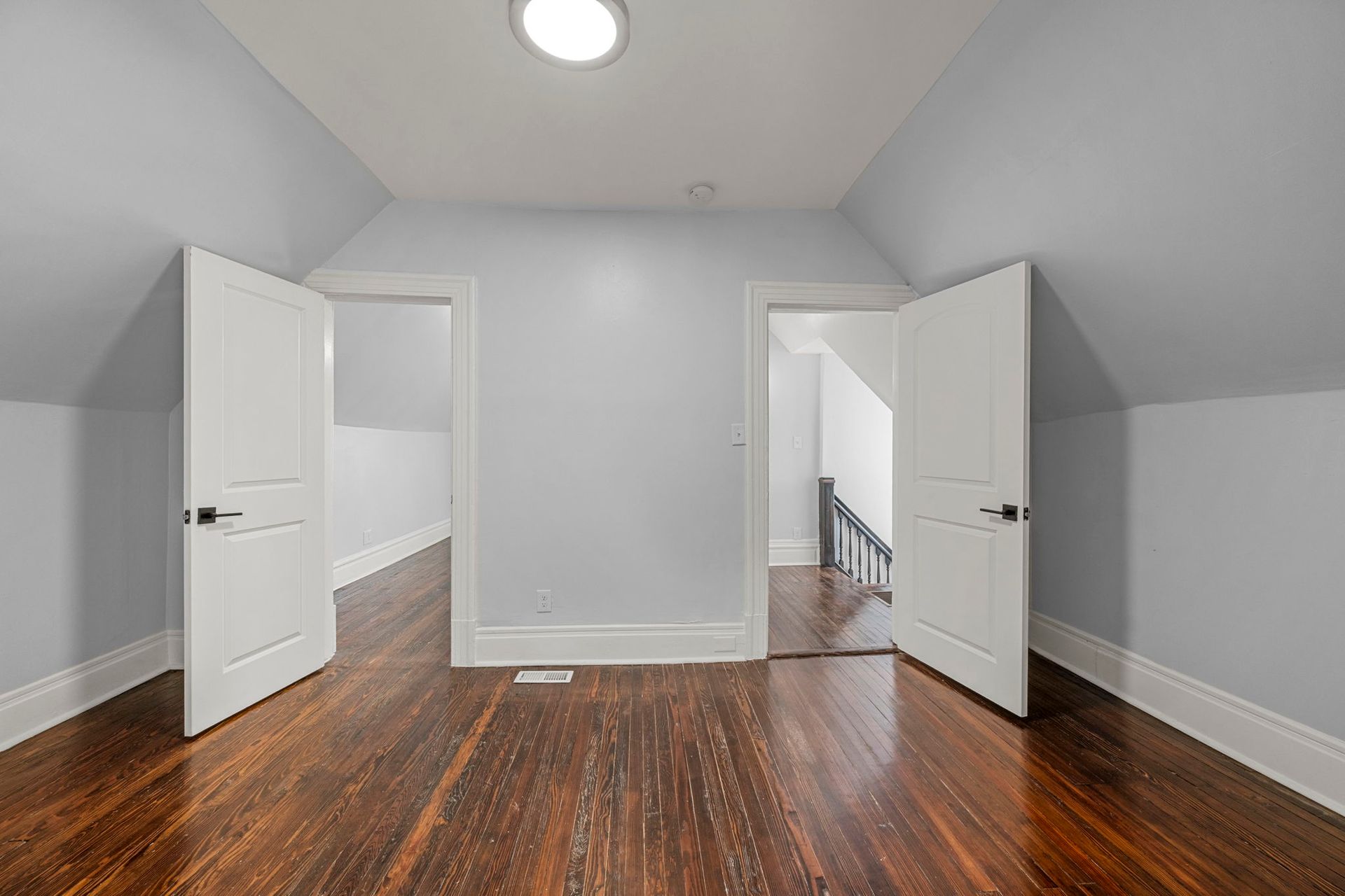 A room with hardwood floors, two open white doors, and light blue walls.