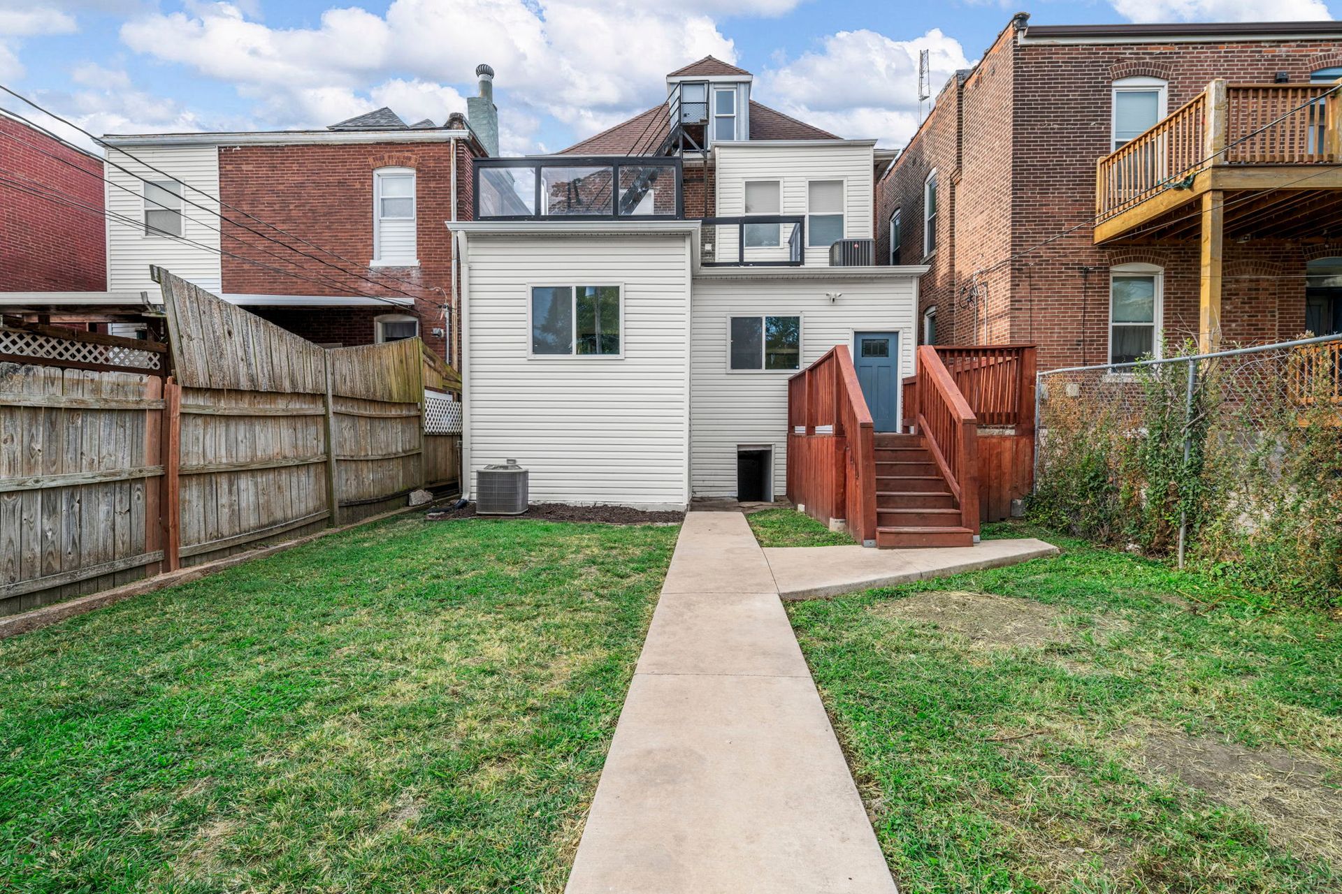 Backyard of a white house with a wooden deck, grass, and a concrete walkway.