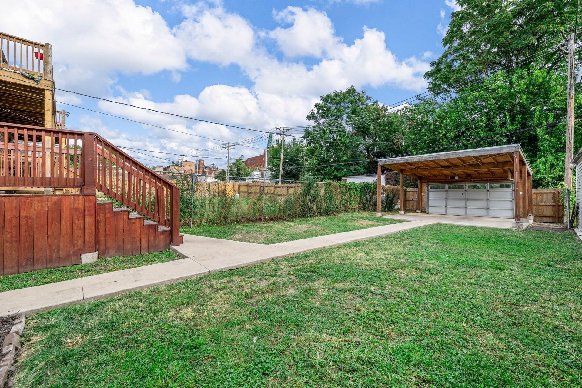 Backyard with wooden deck, garage, and grassy lawn under a cloudy sky.