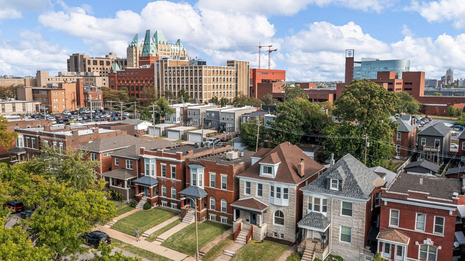 Row of houses in foreground with city buildings in the background under a partly cloudy sky.