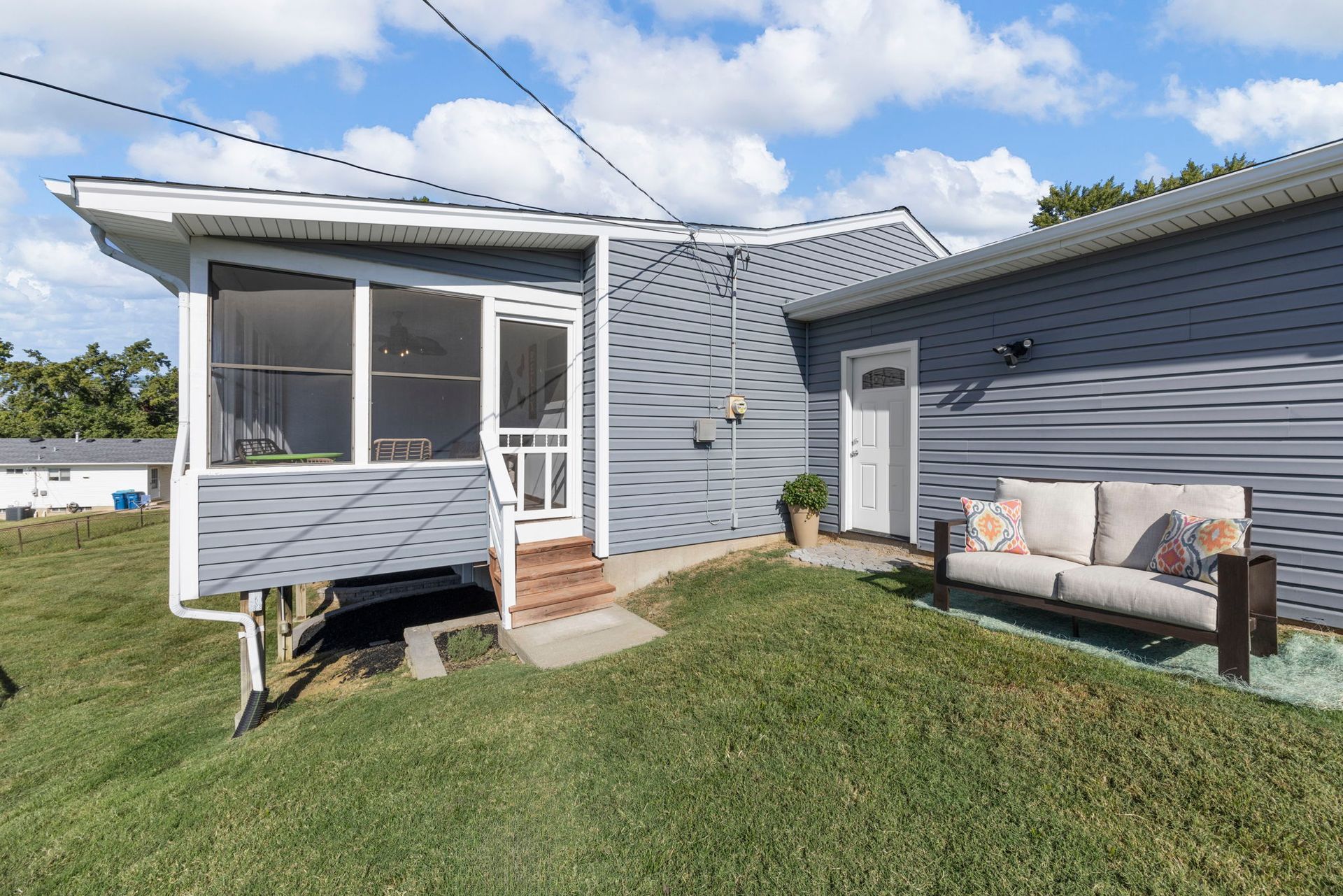 A gray house with a screened porch and outdoor seating on a grassy lawn under a blue sky.