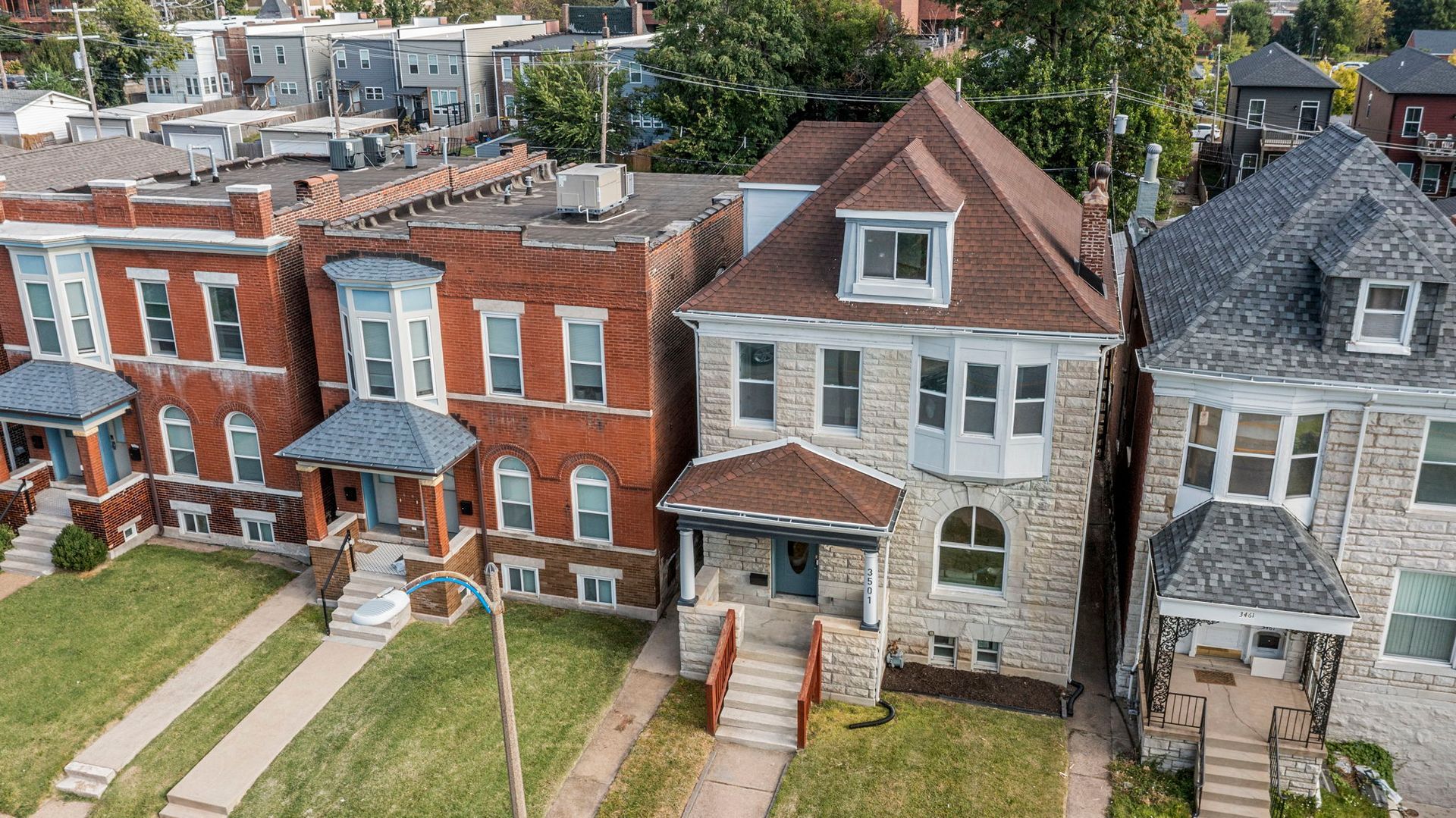 Row of brick and stone houses with front porches and green lawns.
