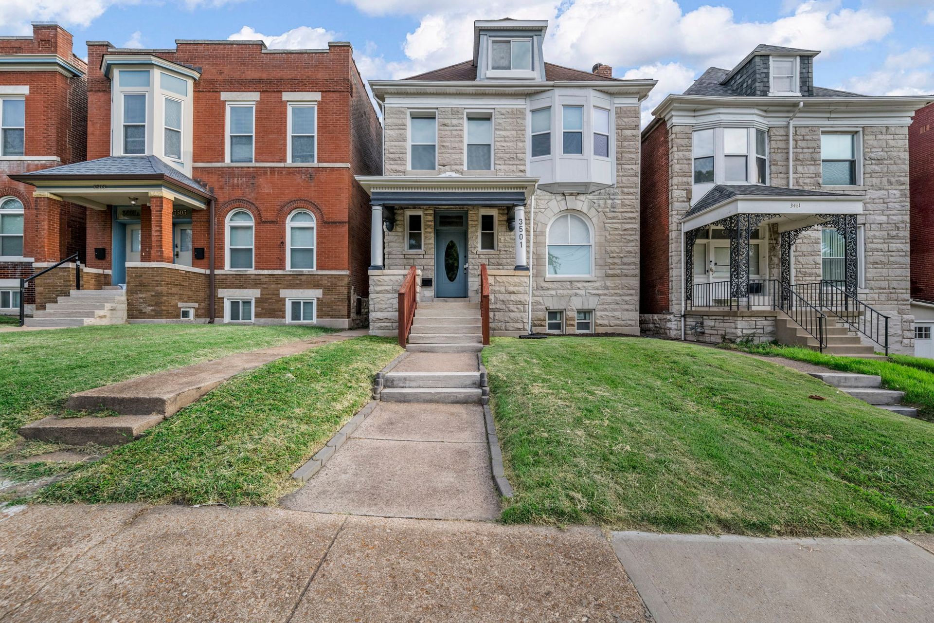 Row of historic brick and stone houses with front lawns and sidewalks on a sunny day.