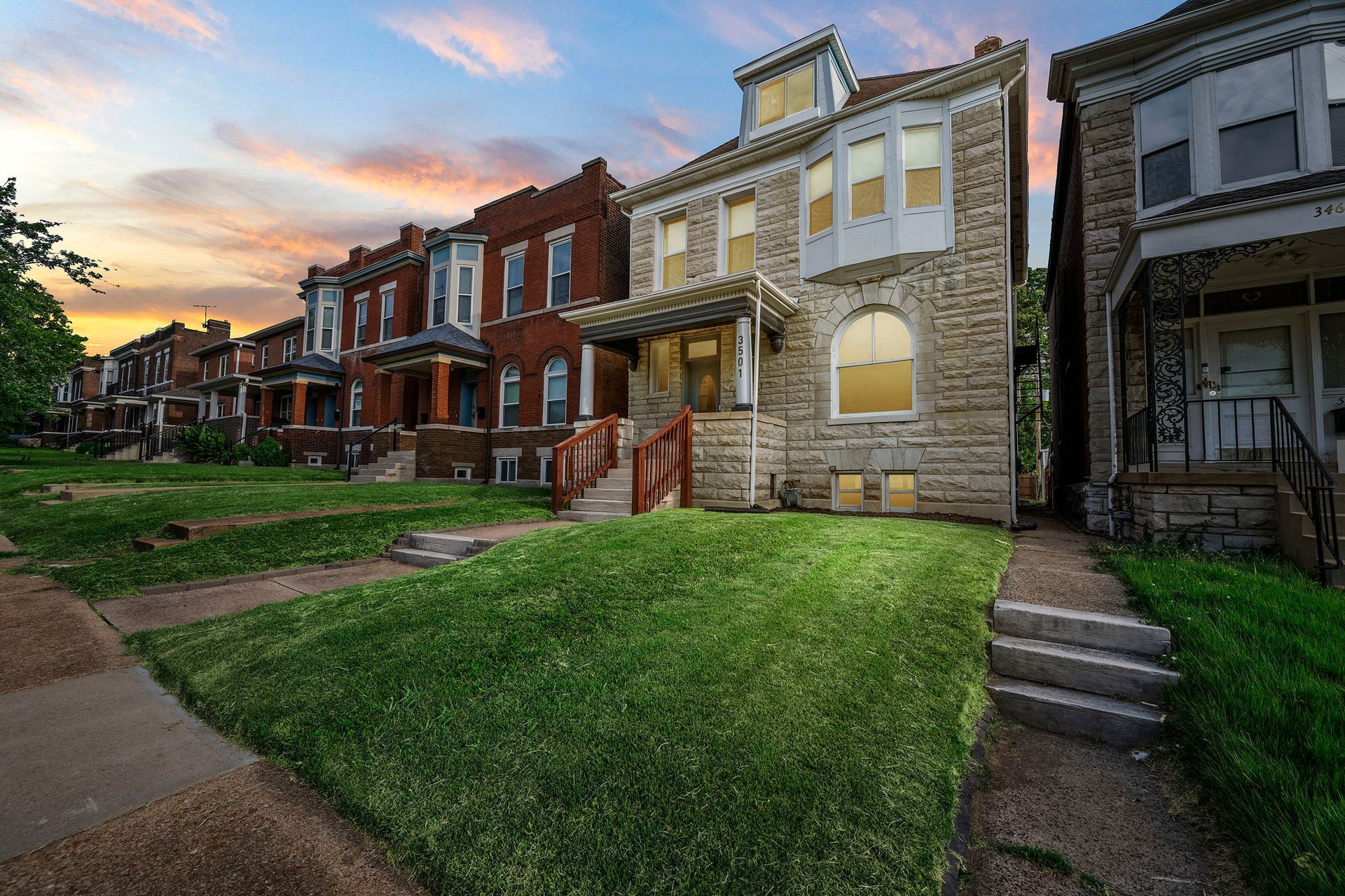 Row of historic brick and stone houses at dusk with lush green lawns.