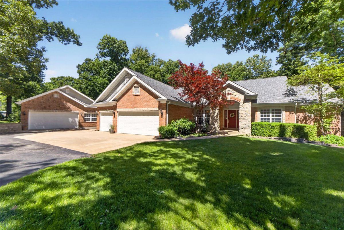 Suburban brick house with three garages, green lawn, and trees on a sunny day