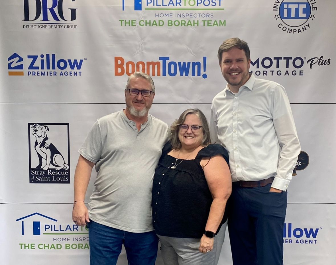 Three people pose in front of a banner with logos. Two men, one woman. Various company logos visible.