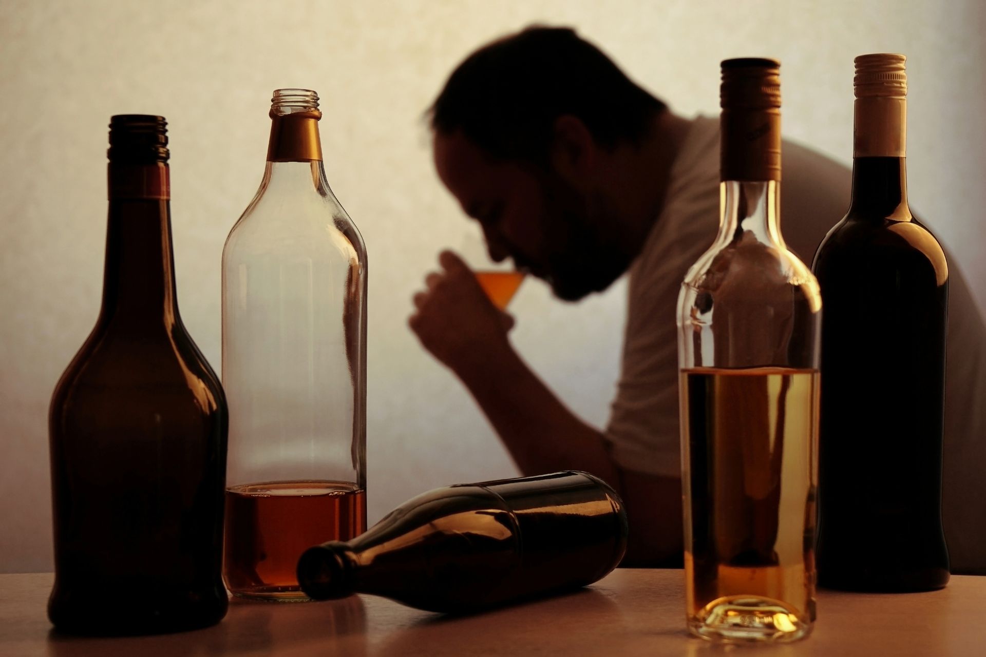 Bottles of alcohol in front of a blurred person drinking from a glass, suggesting alcohol abuse.