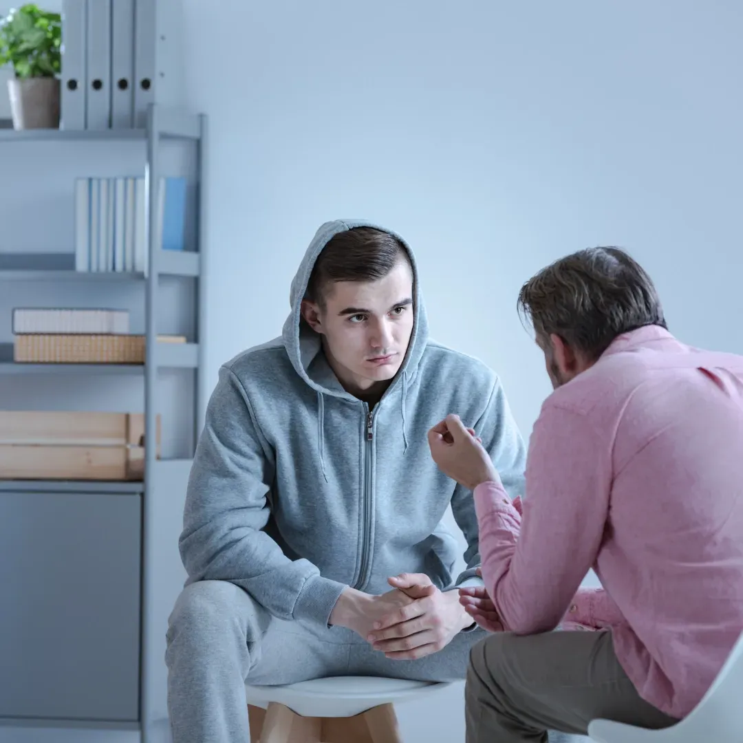 Two men are sitting in chairs talking to each other.