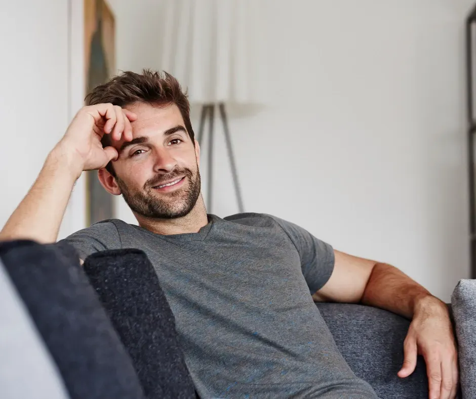 A man is sitting on a couch with his hand on his forehead.