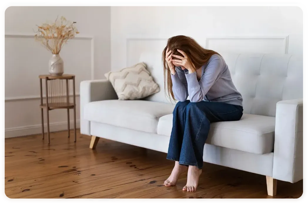 A woman is sitting on a couch with her head in her hands.