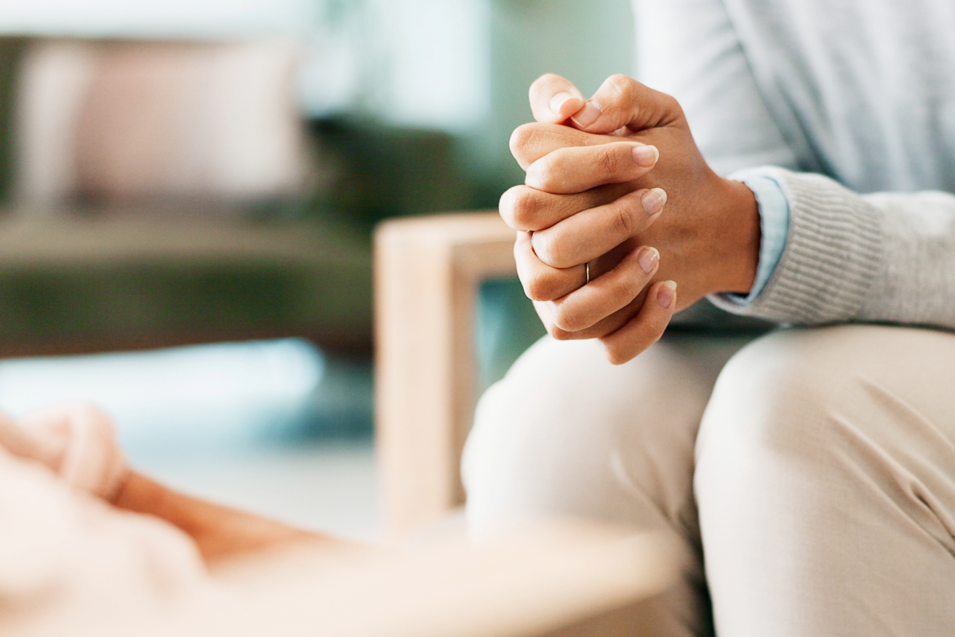 Hands clasped together, resting in lap; person seated indoors, possibly in therapy setting.