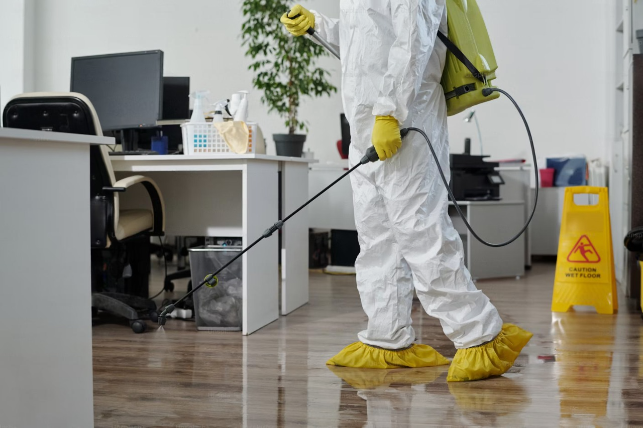 A man in a protective suit is spraying a floor in an office.