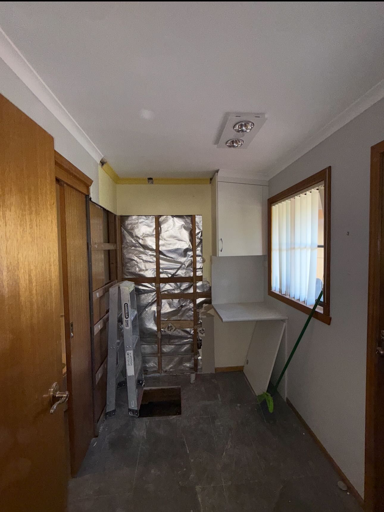 Interior of a room under renovation: exposed wall, cabinet, window with curtain, door, and tools.