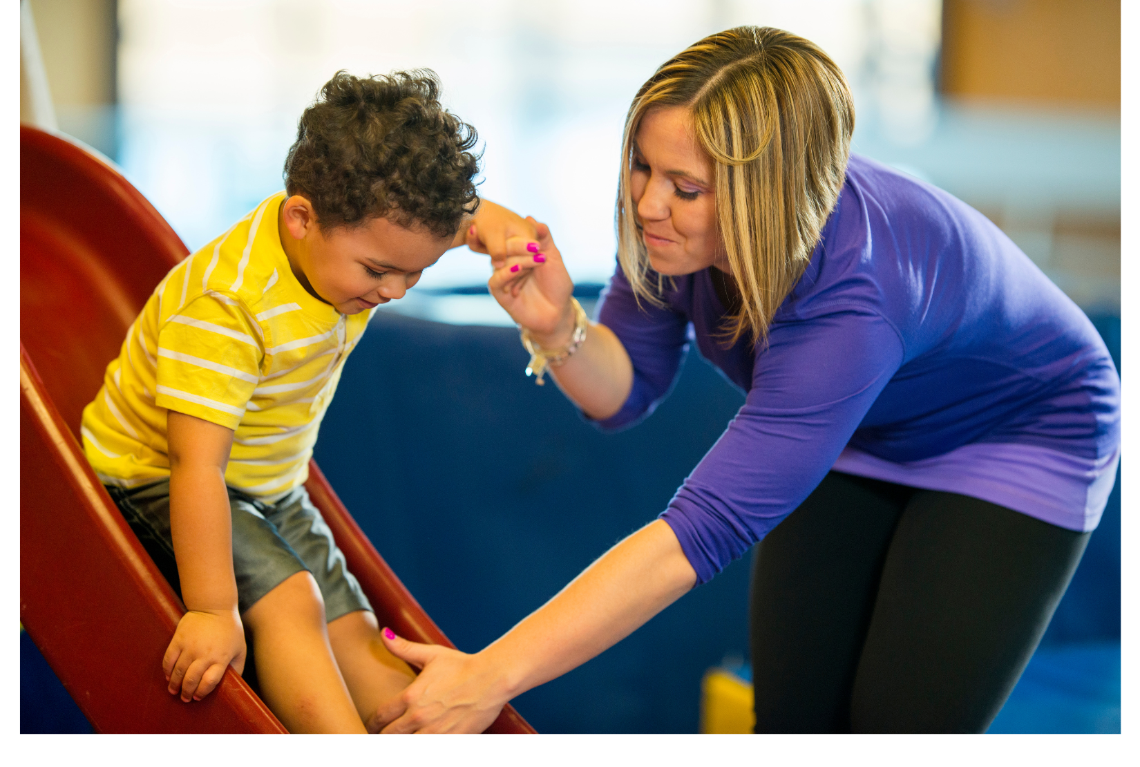 A woman is helping a young boy on a slide.
