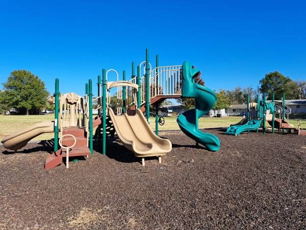 Playground with tan, green, and brown slides on a sunny day.