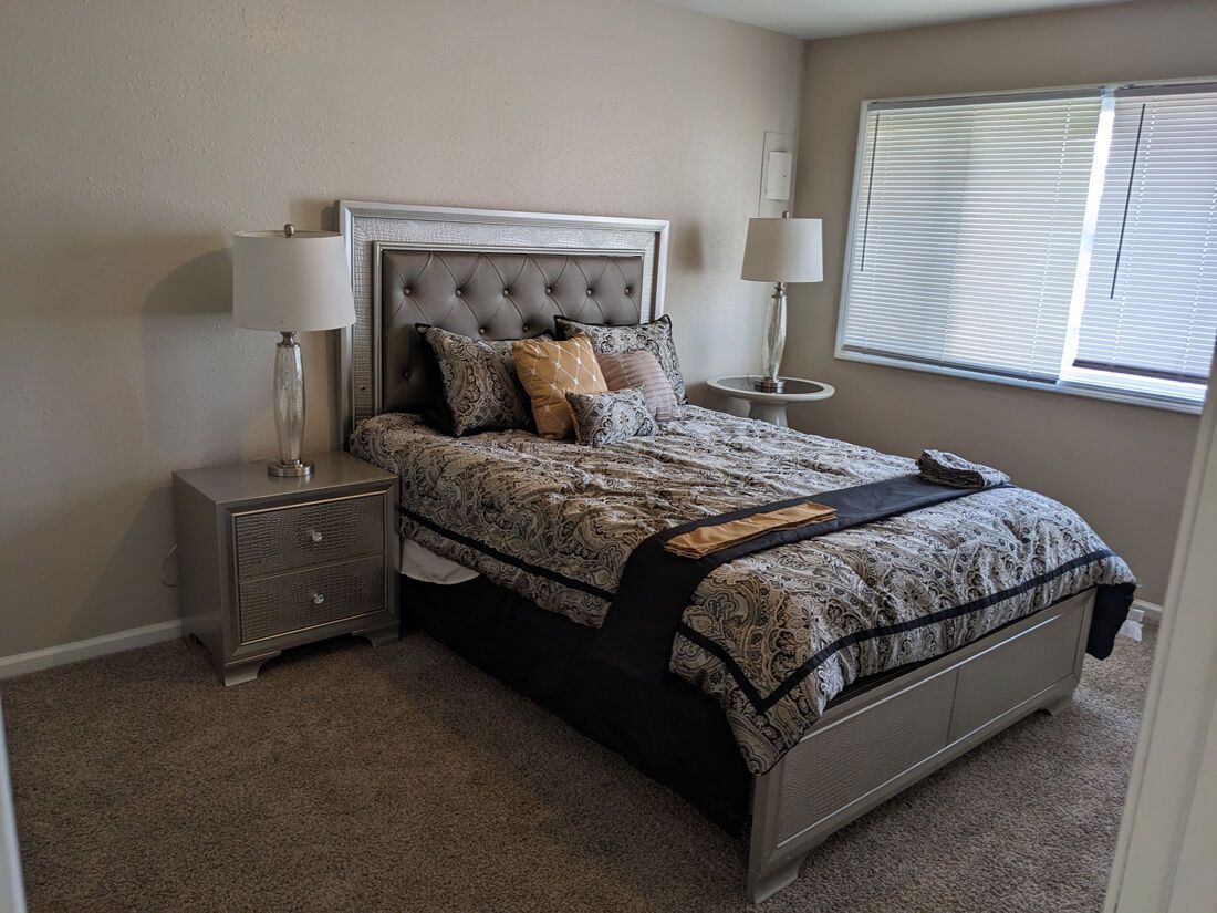 Bedroom with a bed, two nightstands, two lamps, and a window with blinds.