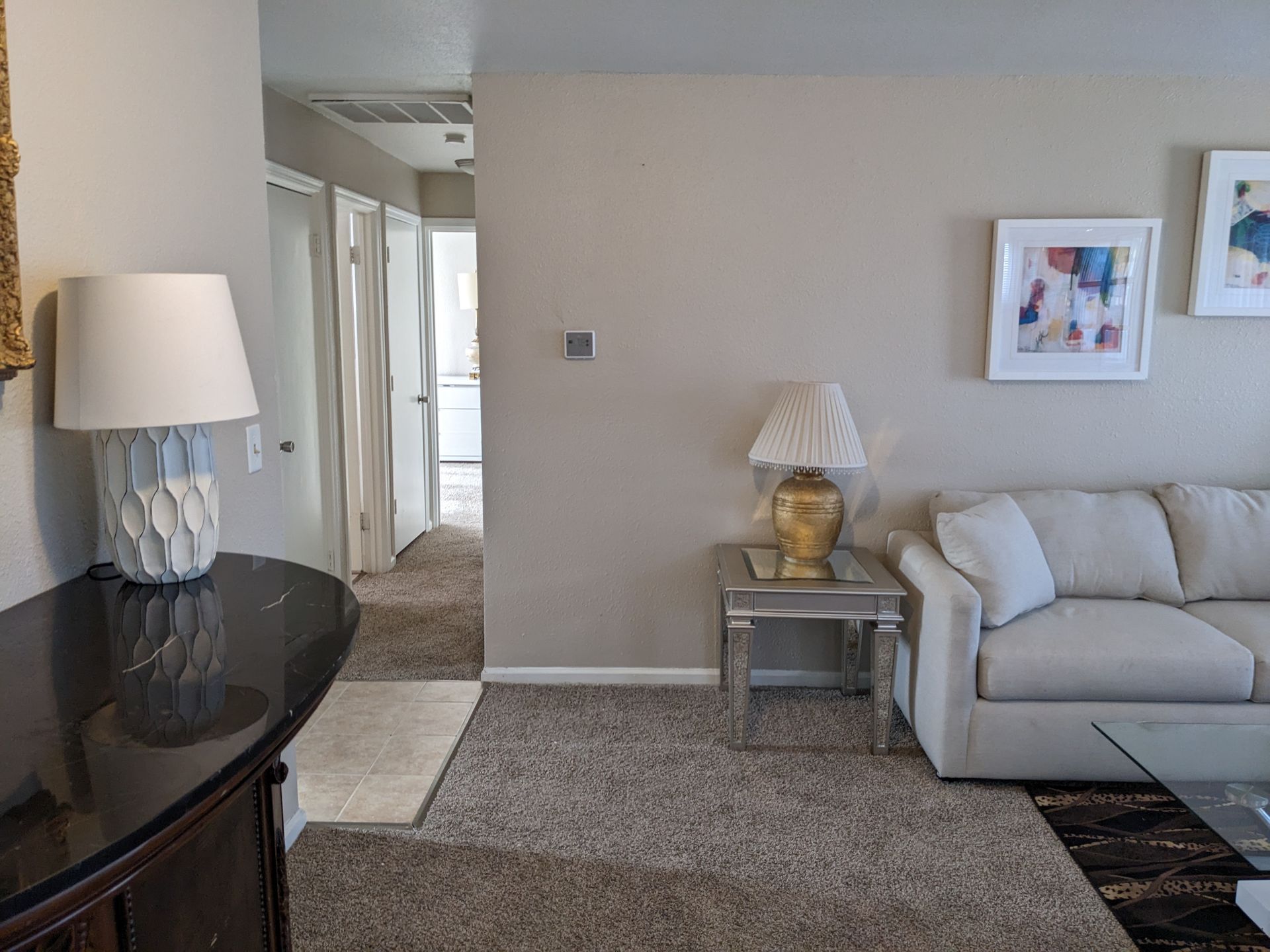 Living room with beige walls, sofa, rug, lamps, and hallway leading to other rooms.