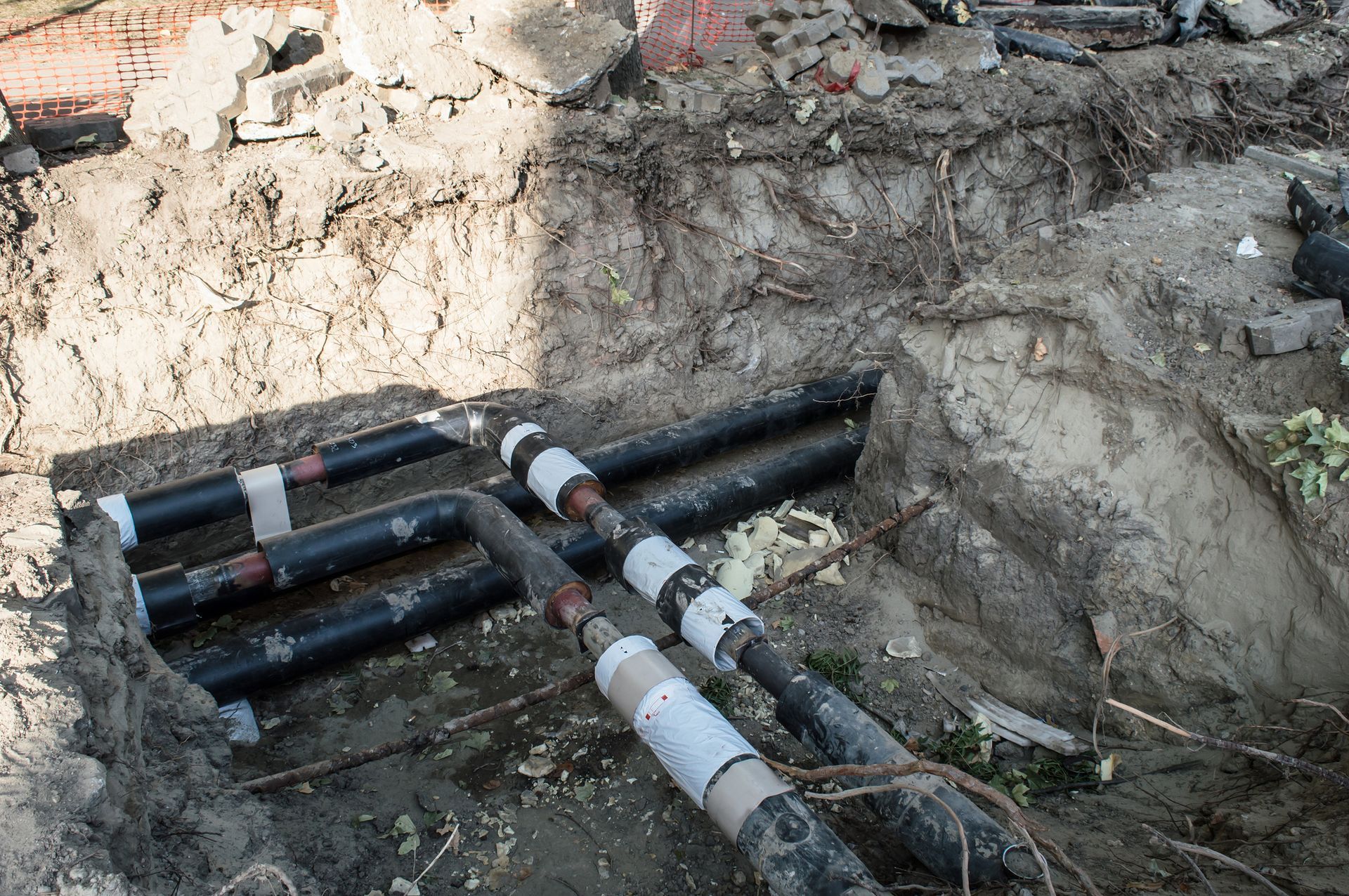 Pipes in a trench. Black pipes wrapped in insulation are visible in the dirt.