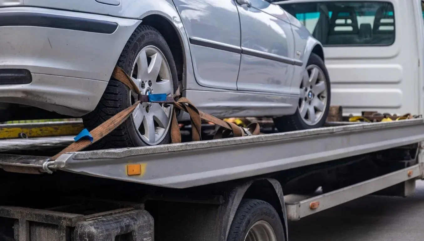 Silver car strapped to a flatbed tow truck, with another white vehicle behind it.