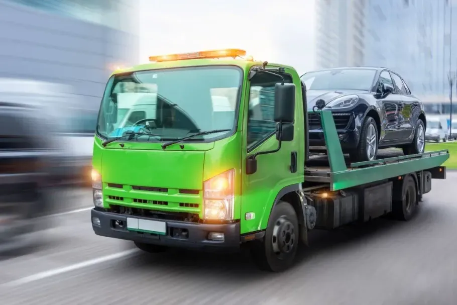 Bright green tow truck hauling a black SUV on a flatbed, driving on a blurred road