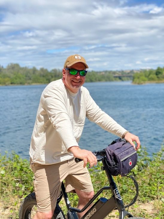 A man is riding an electric bike next to a body of water.