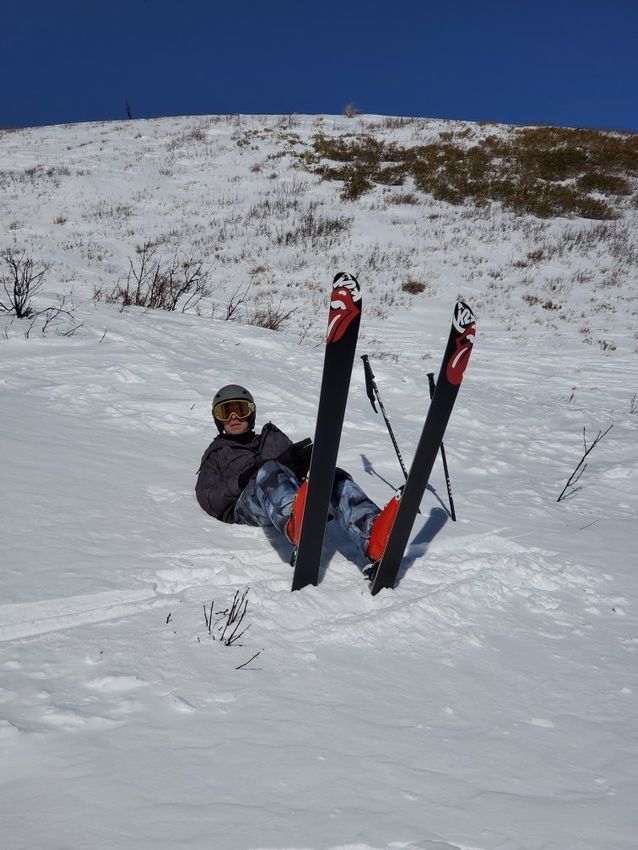 A person is laying on their back in the snow with their skis upside down.