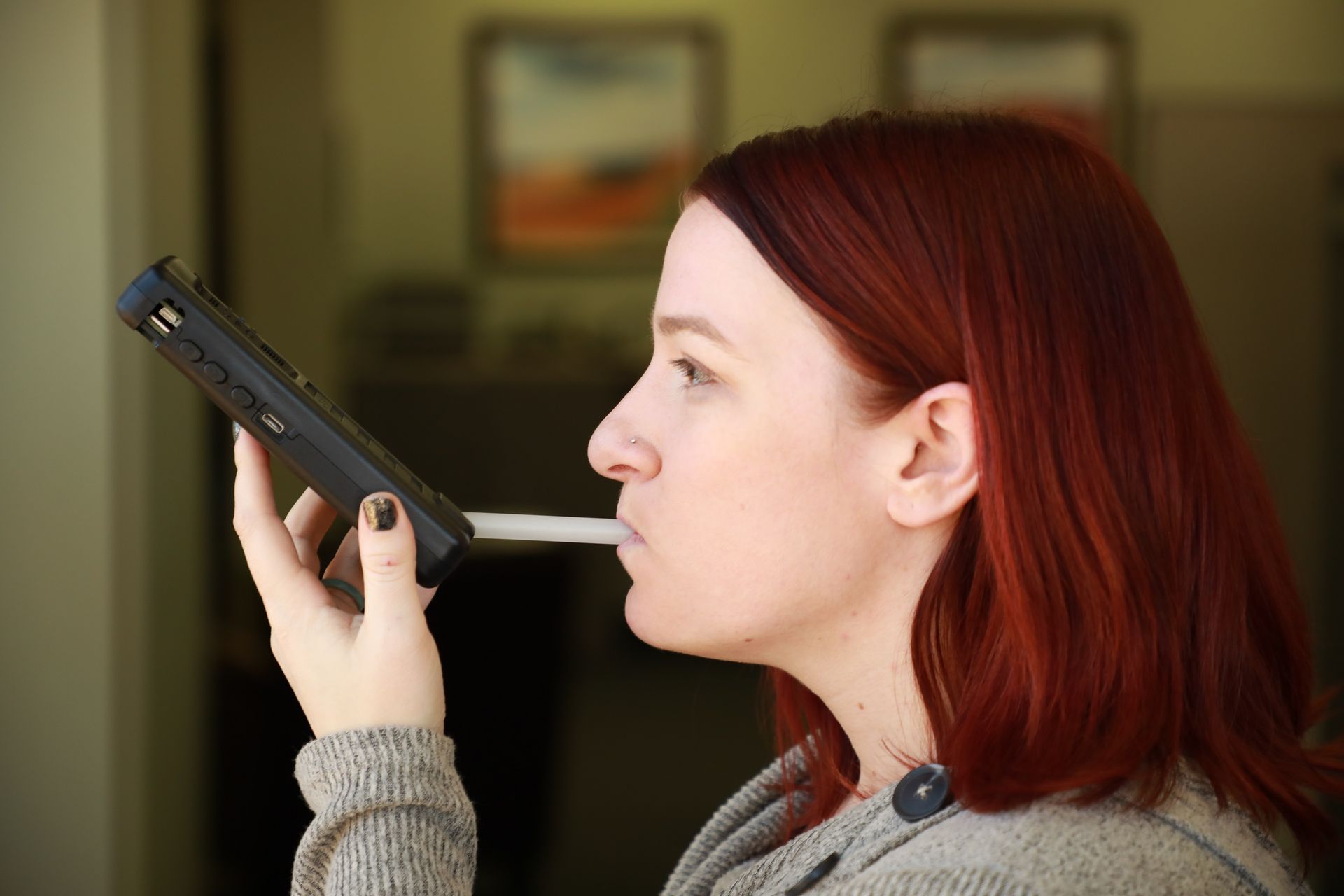 Person using a handheld device near their mouth, side profile indoors with a blurred background.