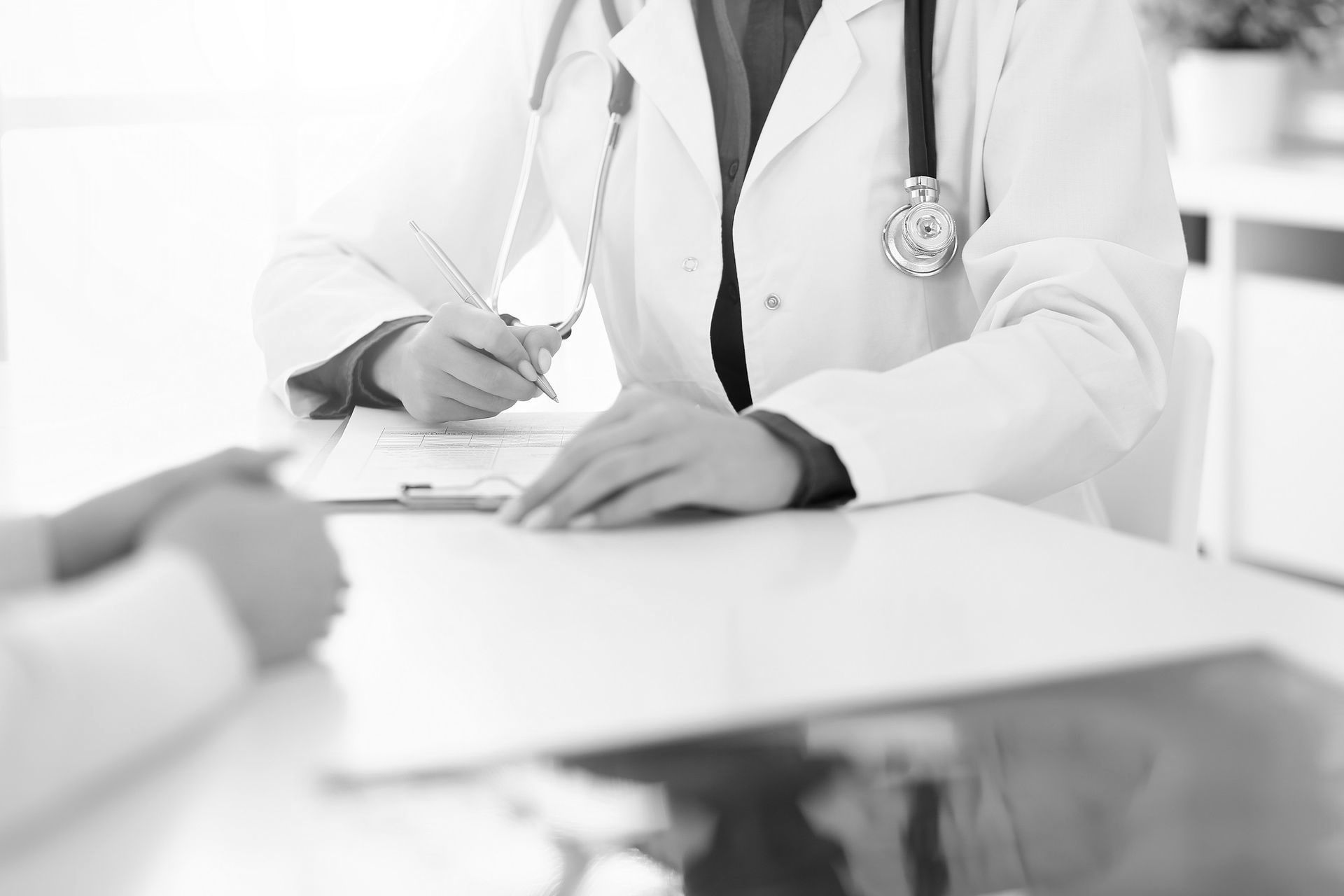 Doctor writing on a clipboard, meeting with a patient in a medical office.