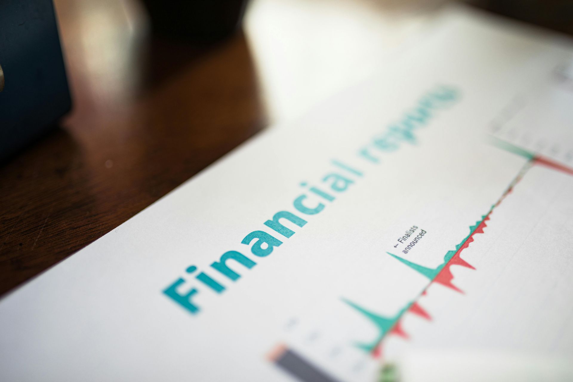 Financial report with a teal title and red line chart on a white page on a wooden desk