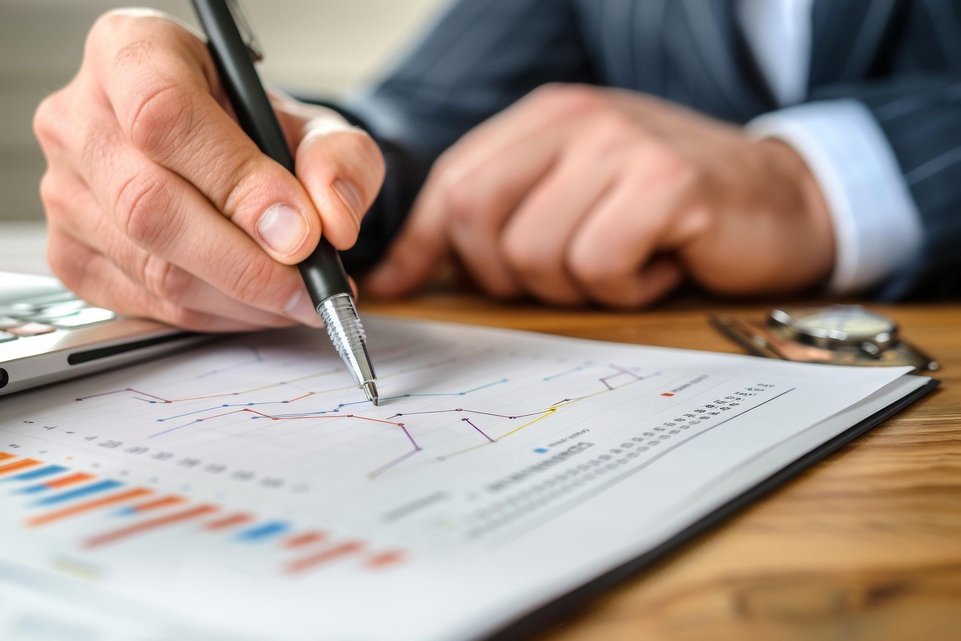Hand holding a pen over financial charts on a clipboard at a desk