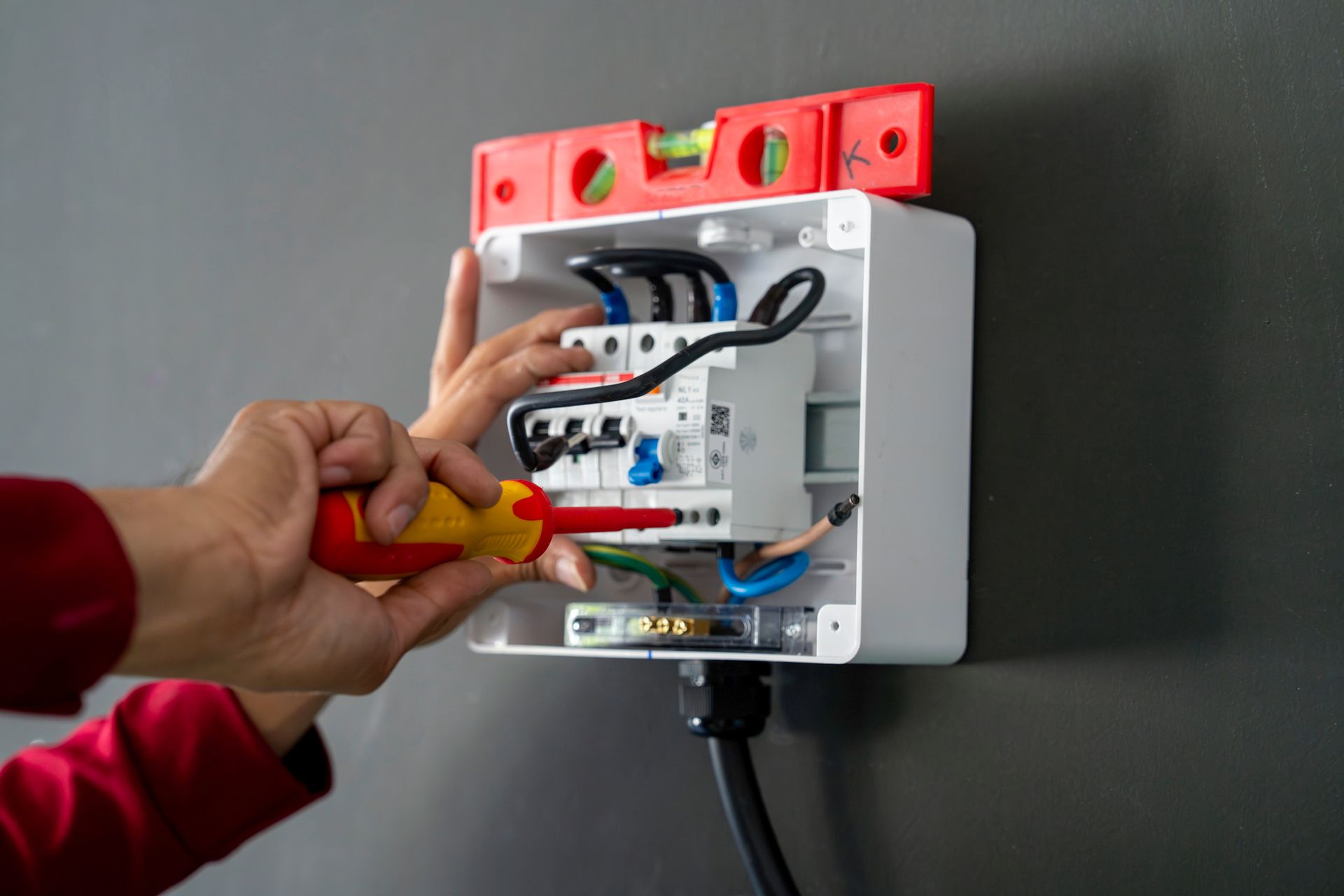 A person is using a screwdriver to fix an electrical box on a wall.
