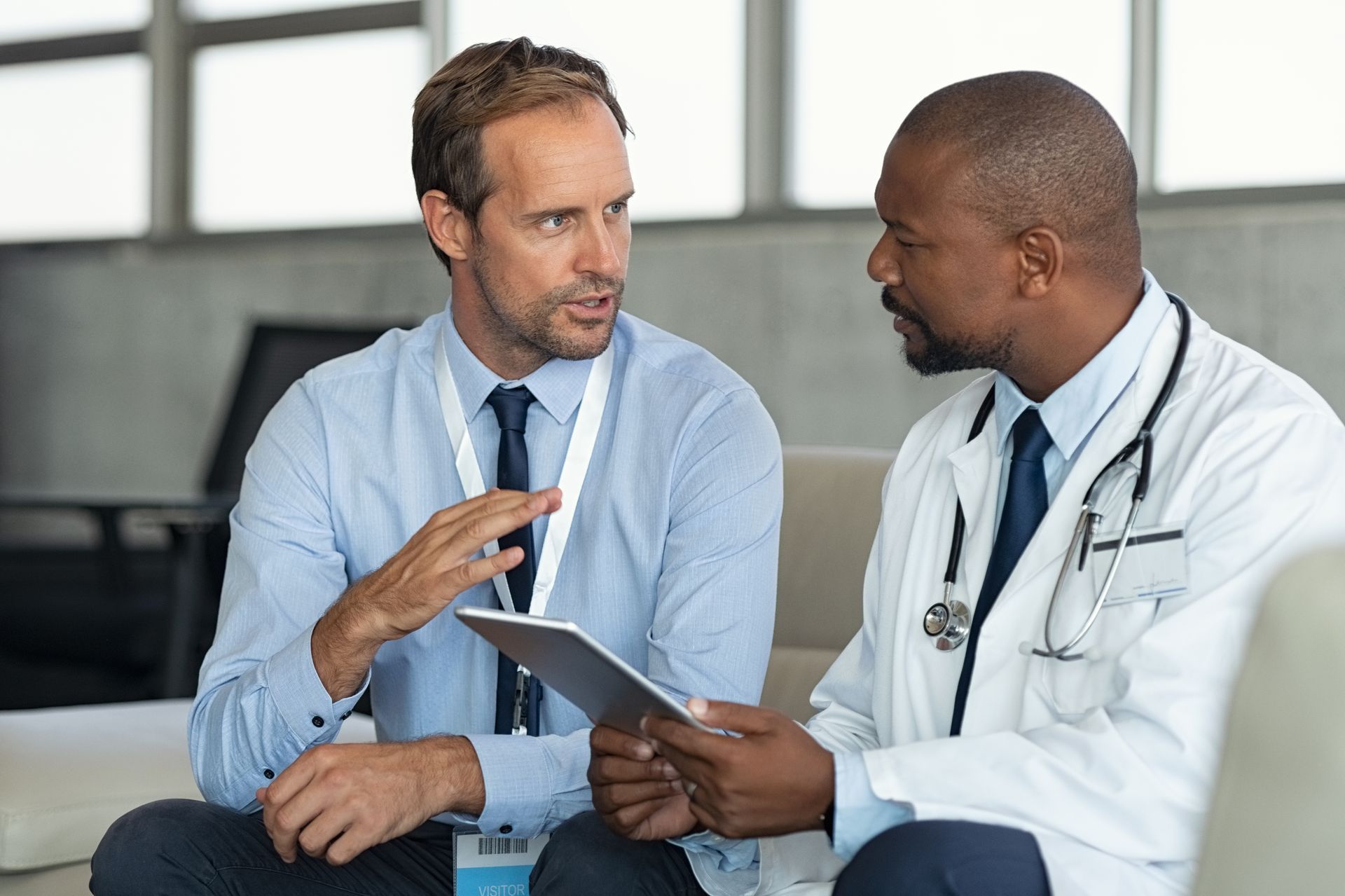 A doctor is talking to a man while holding a tablet.